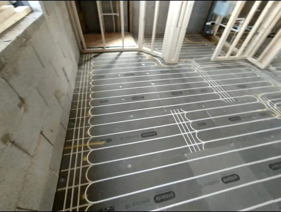 Low-profile wet underfloor heating pipework laid on cementitious boards next to exposed blockwork wall and timber studs