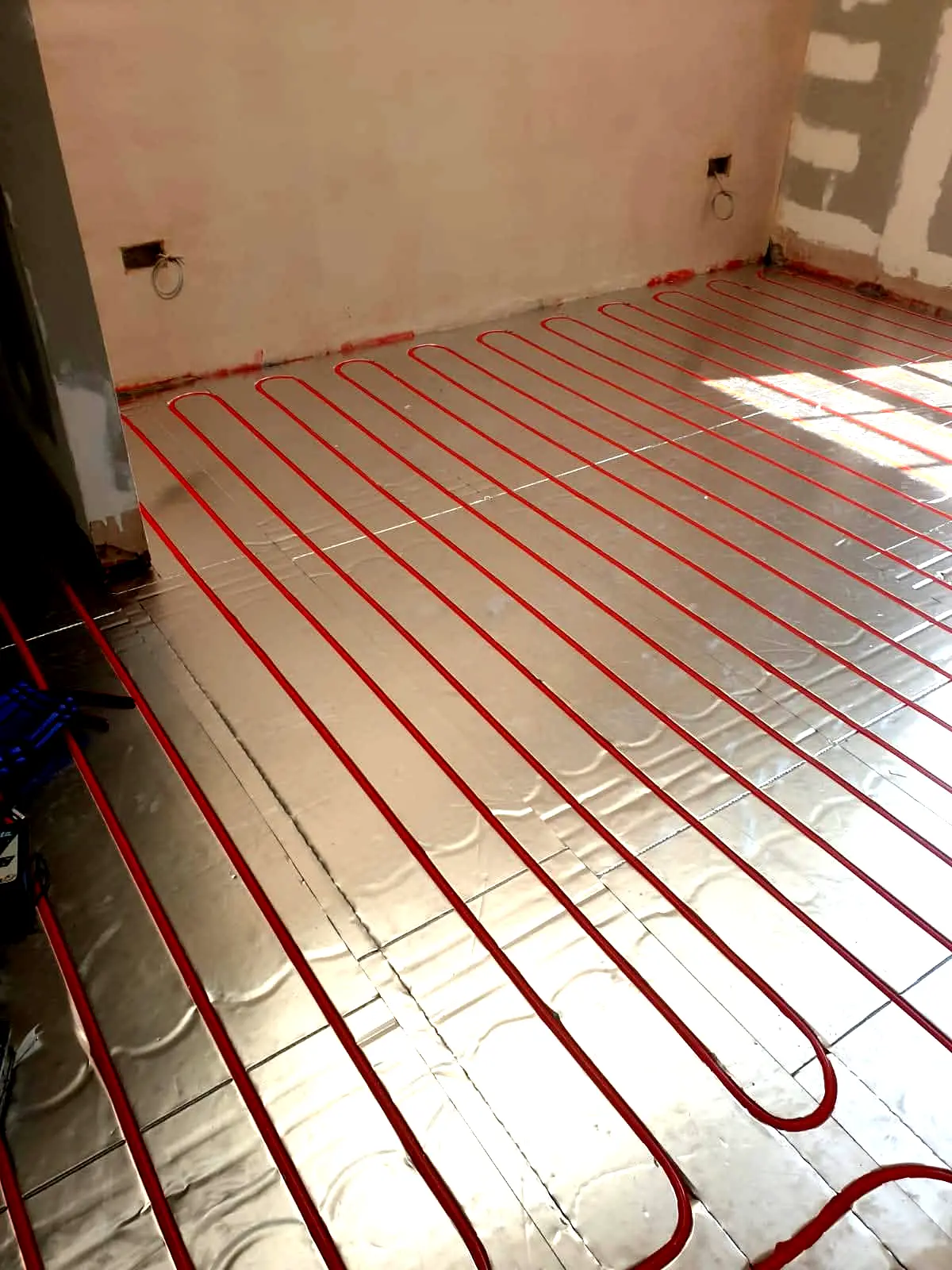 Red underfloor heating pipes installed over silver foil insulation in new build room at Cedar Close, Bristol