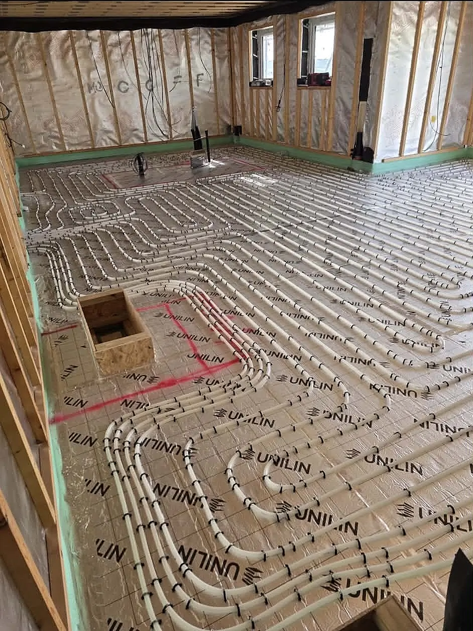 Construction view of a long room with timber stud walling and underfloor heating pipe loops on foil insulation