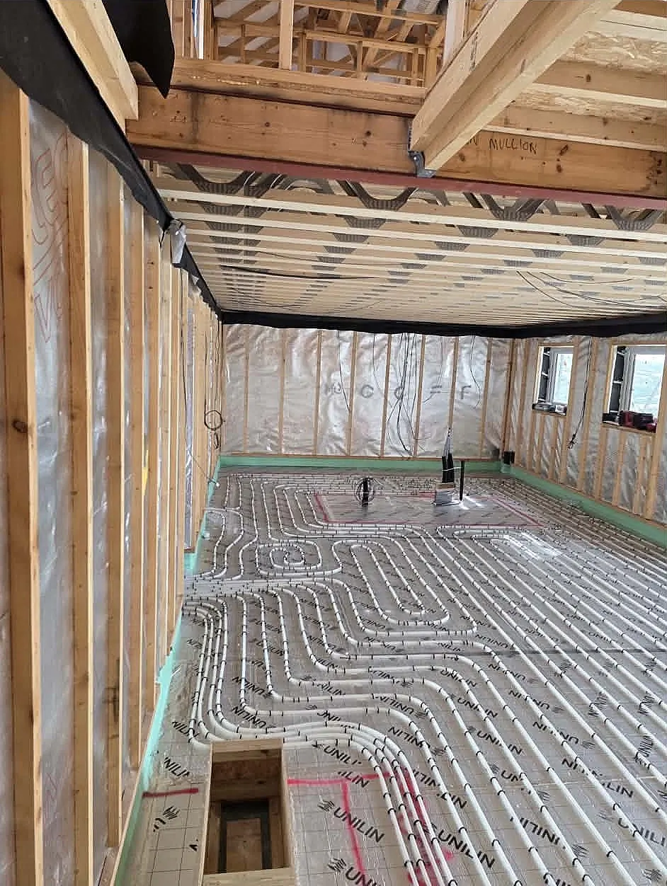 Corner view of a timber-framed room showing installed underfloor heating pipes prior to screeding at Lakeside Villa
