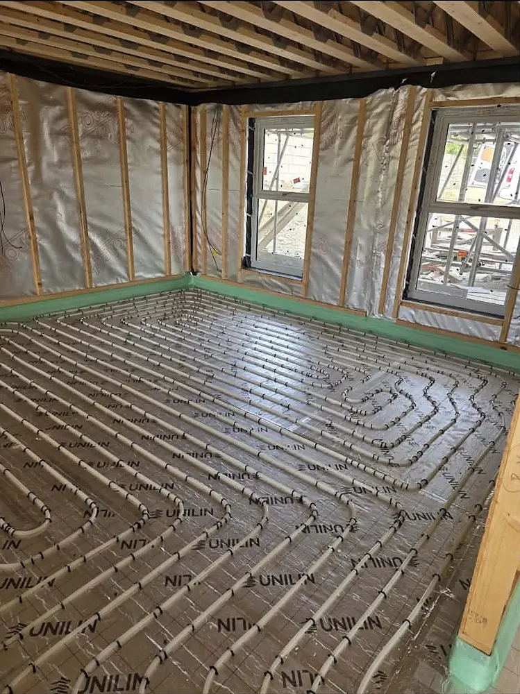 Timber-framed room under construction with wet underfloor heating pipework laid out over silver insulation