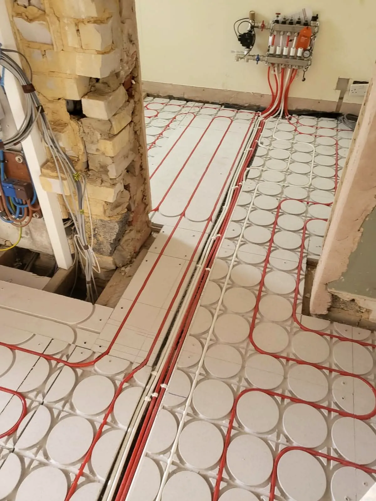 Underfloor heating pipe loops installed in room corner over white insulation panels, Sandbanks Road project