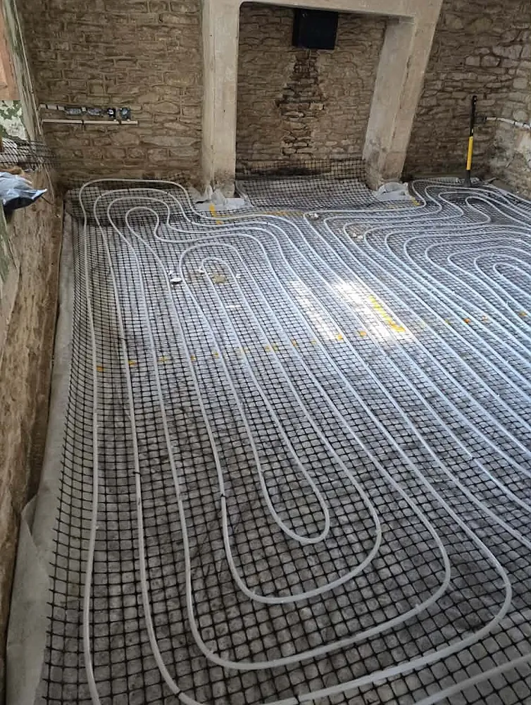 Overhead view showing complete white underfloor heating pipe layout on grid mesh insulation inside stone cottage