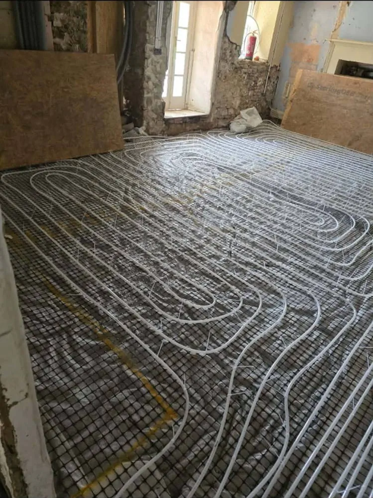 White underfloor heating pipes laid in a spiral pattern on mesh insulation mat during stone cottage extension renovation