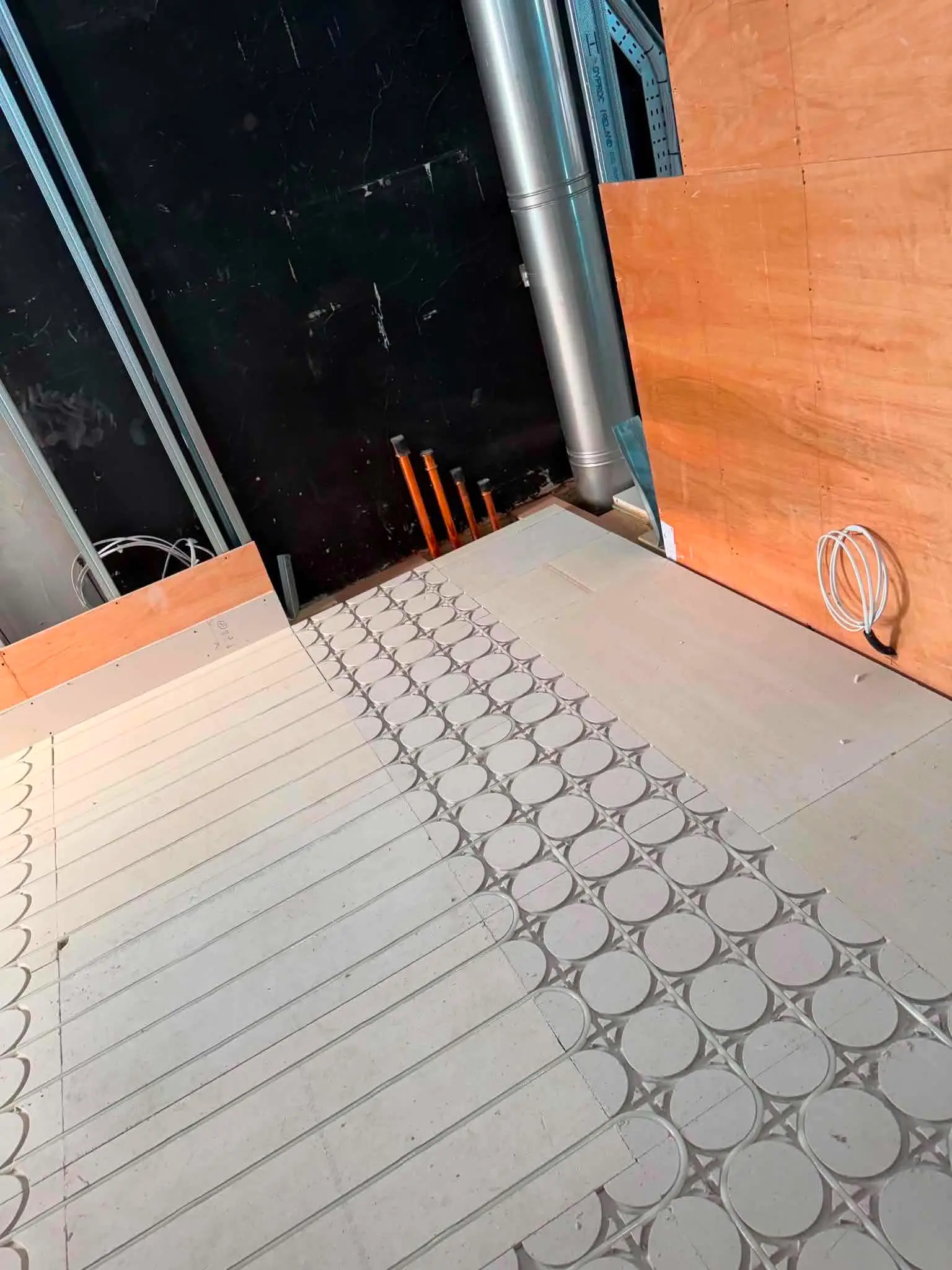 Close-up view of castellated underfloor heating panels and copper pipe feeds near internal partitioning, Kensington project