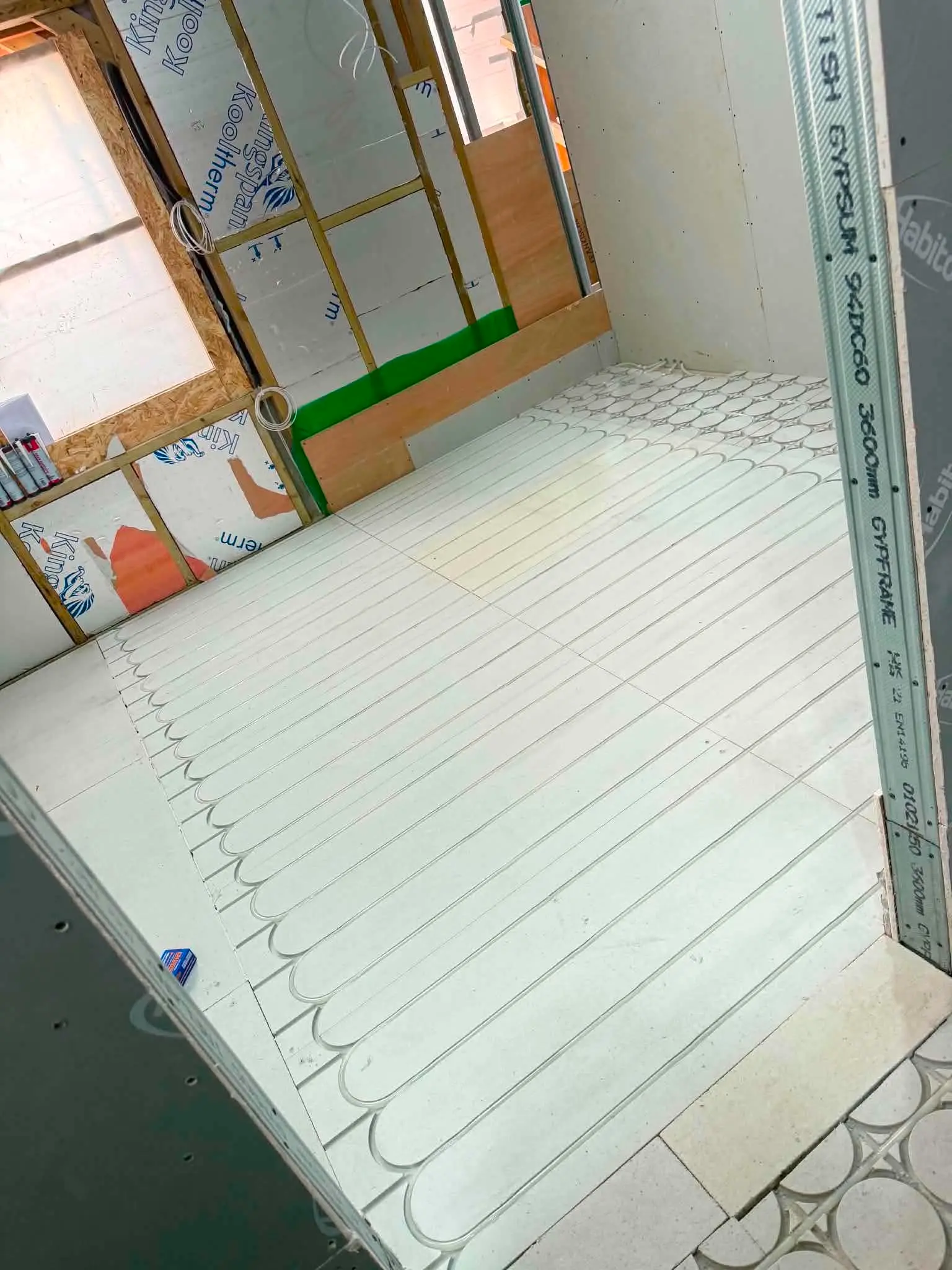 Perspective view down a long penthouse corridor showing castellated floor insulation installed alongside metal stud framing