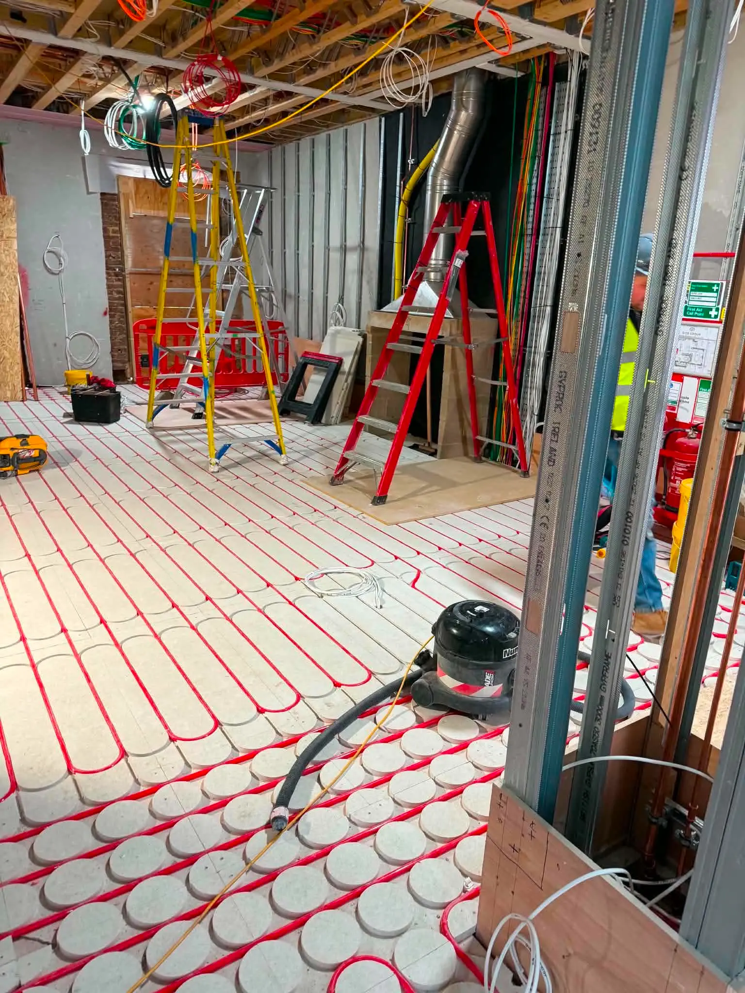 Spacious room under renovation showing red wet underfloor heating pipes laid on castellated panels at The Kensington Crown Penthouse