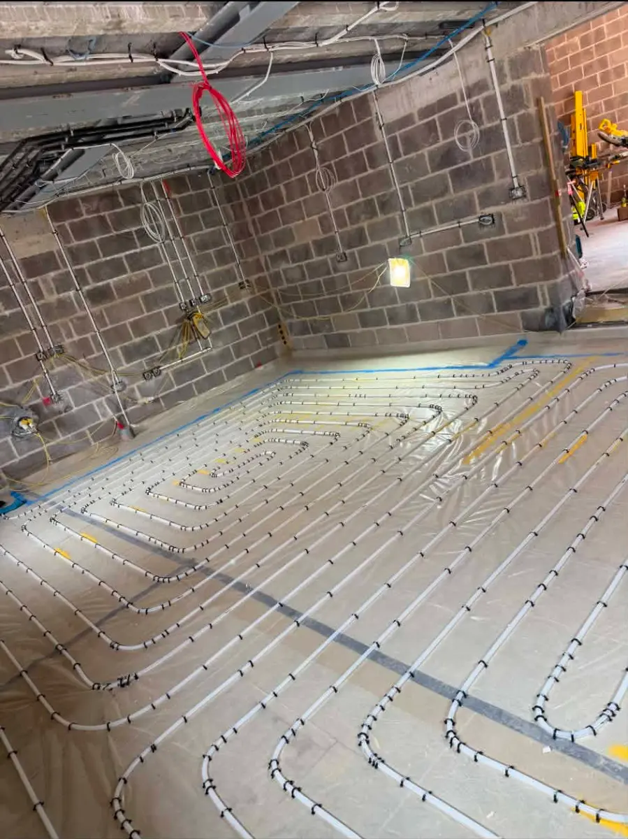 Corner view of underfloor heating pipe layout on insulation boards against blockwork walls, Oakwood Residence project