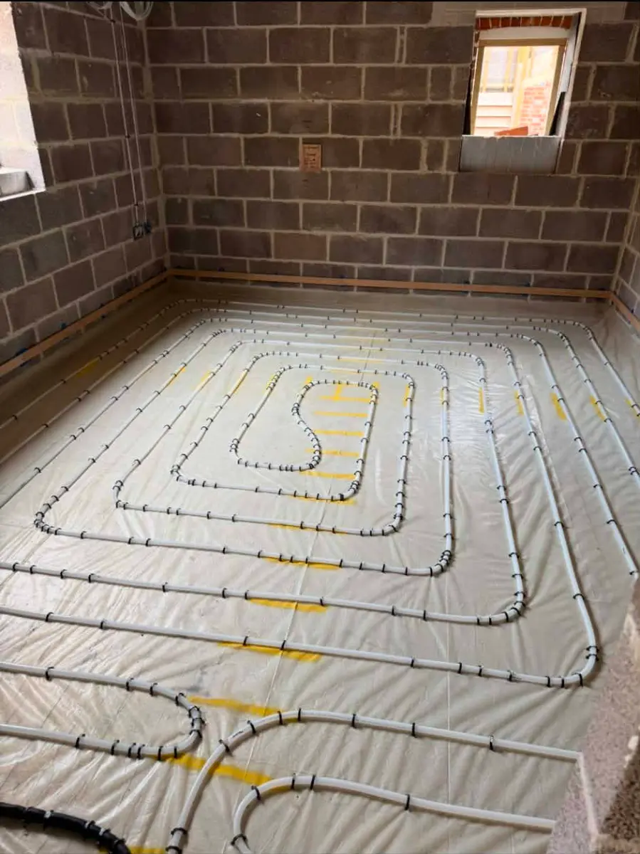 Close-up of black conduits protecting underfloor heating manifold pipe feeds in a utility room at Oakwood Residence