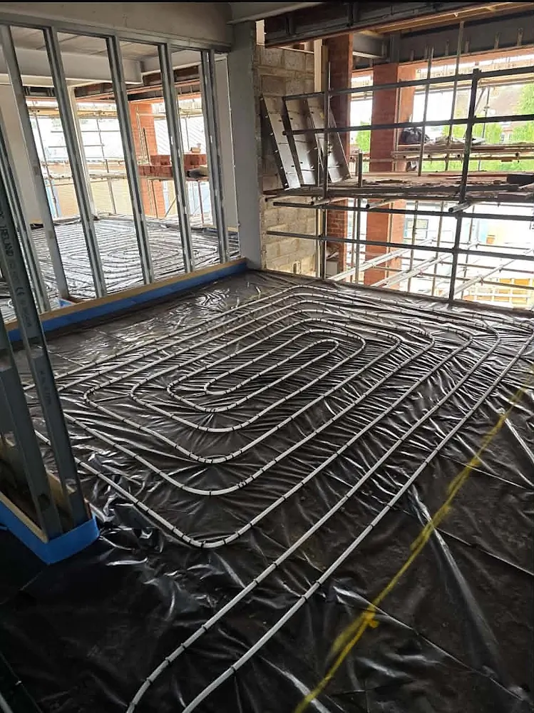 Wet underfloor heating pipes laid on black insulation membrane within steel frame construction at Westbrook Academy