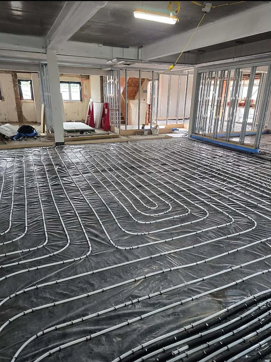 Interior construction view showing wet underfloor heating pipe loops across concrete floor and metal partition studs