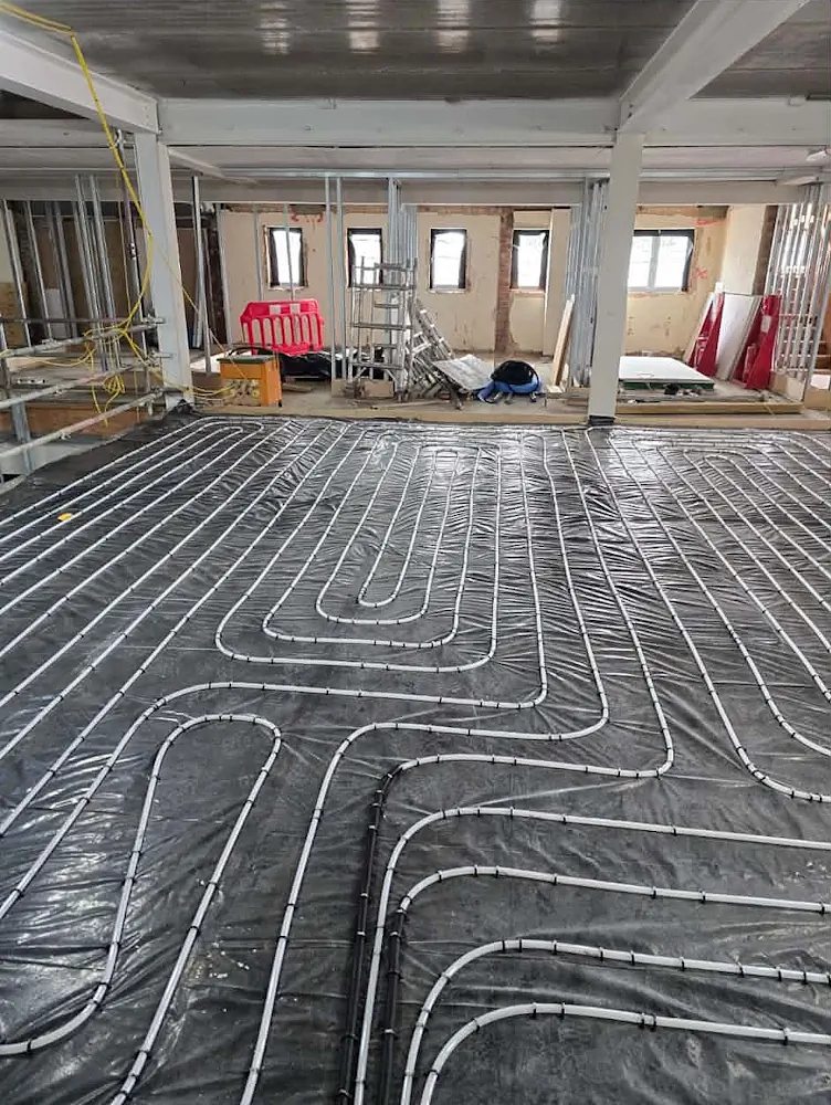 Overhead view of extensive wet underfloor heating pipe layout on black membrane insulation during school construction