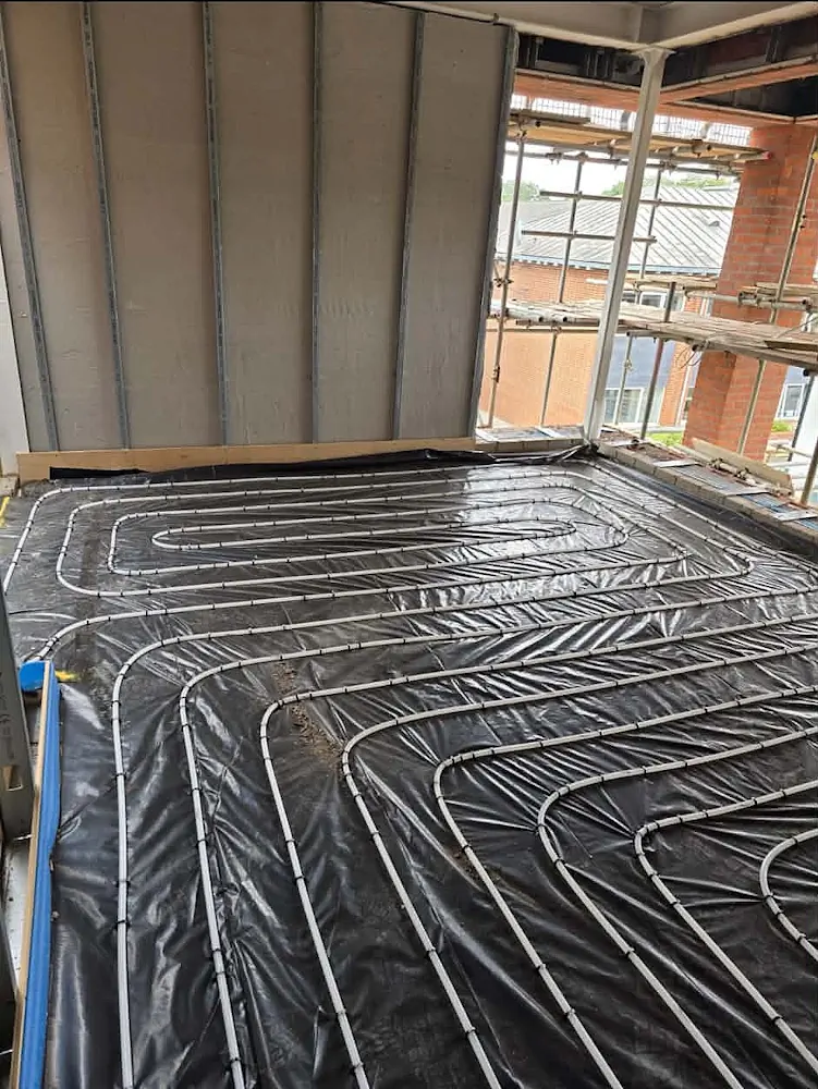 Open floor space showing underfloor heating pipe layout between structural concrete pillars in commercial school building